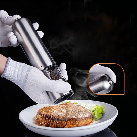 Gloved hands using a stainless steel electric pepper grinder over a steak.