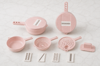 A set of pastel pink plastic kitchen utensils and accessories arranged on a light marble surface, including a small pot, bowl, strainer, colander, grater, and several blade attachments.
