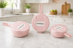 Three pink plastic kitchen utensils with round lids and handles, displayed on a white marble countertop in a bright, modern kitchen setting.