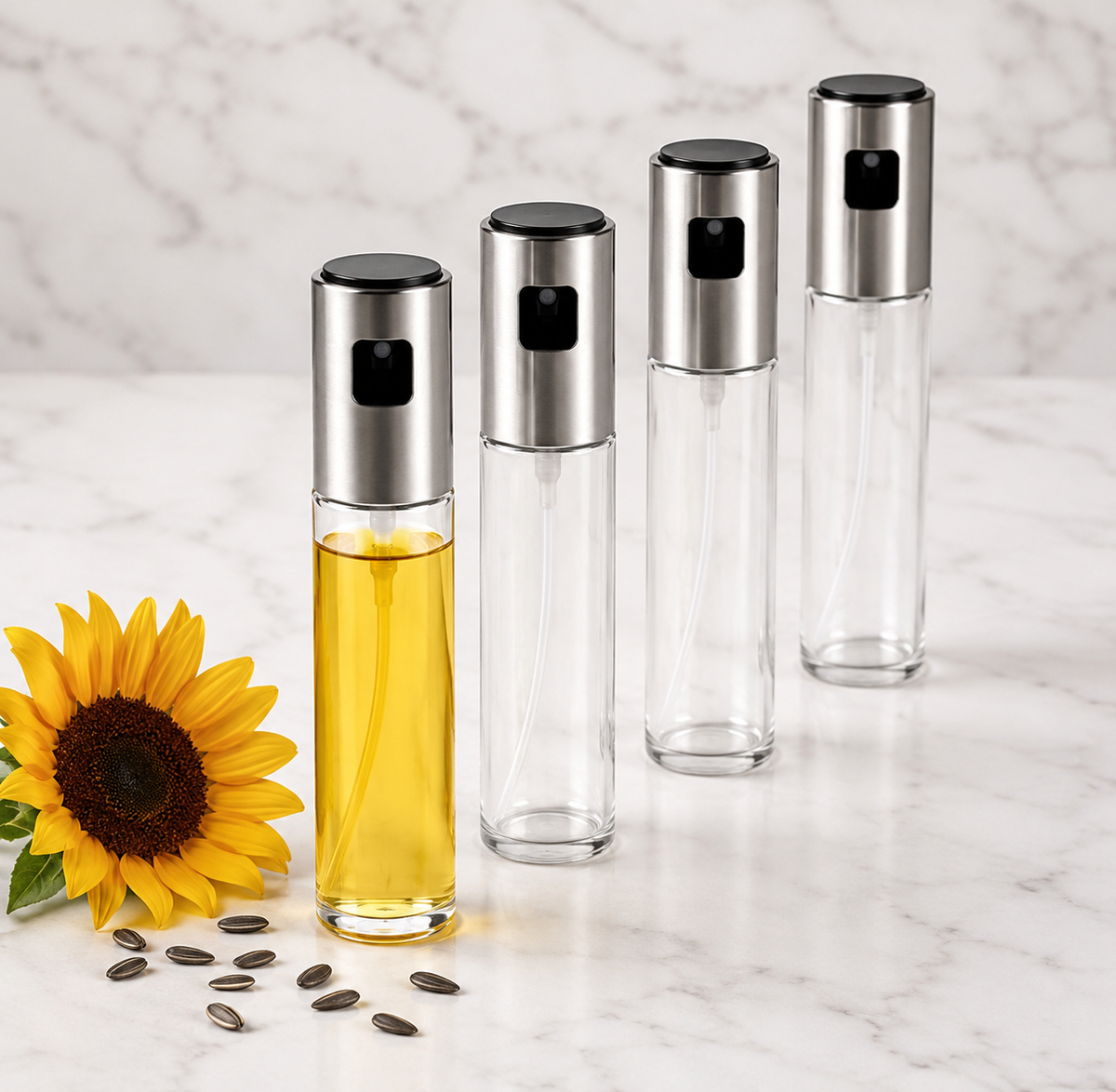 Four clear glass oil bottles with silver metal spray caps are arranged on a white marble surface. One bottle is filled with yellow oil, and a yellow sunflower with scattered seeds sits beside it.