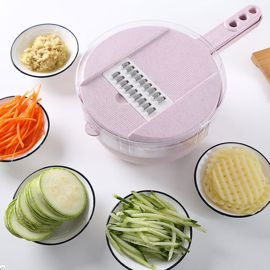 Pink vegetable slicer with a clear bowl surrounded by sliced and shredded vegetables.