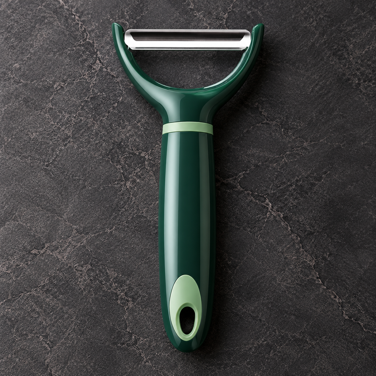 A dark green peeler with a silver metal blade, resting on a dark gray textured stone surface.