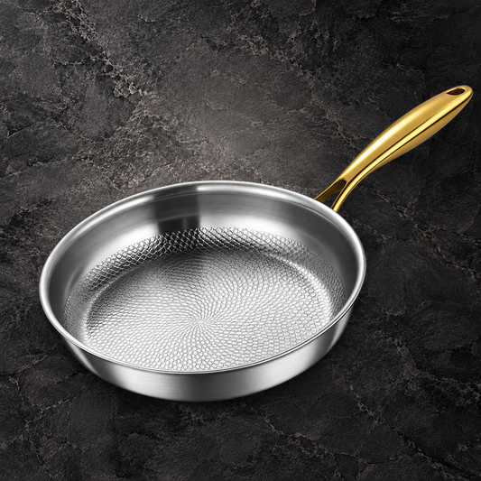 Silver-colored frying pan with a textured cooking surface and gold-colored handle on dark stone.