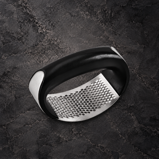 Rocking garlic press with a black curved handle and perforated stainless steel plate on dark stone.
