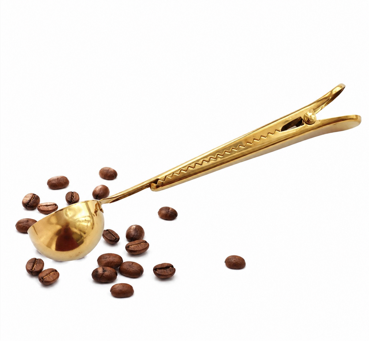 A gold-colored metal coffee scoop with a spring-loaded clip handle, shown with scattered coffee beans on a plain white background.