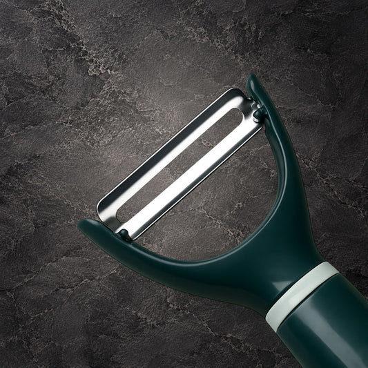 A close-up of a dark green peeler with a silver metal blade and a white accent ring, set against a dark textured stone background.